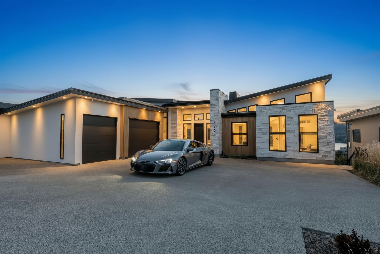 Contemporary single-storey home with stone accents, garage lighting and a sports car in the driveway at blue hour