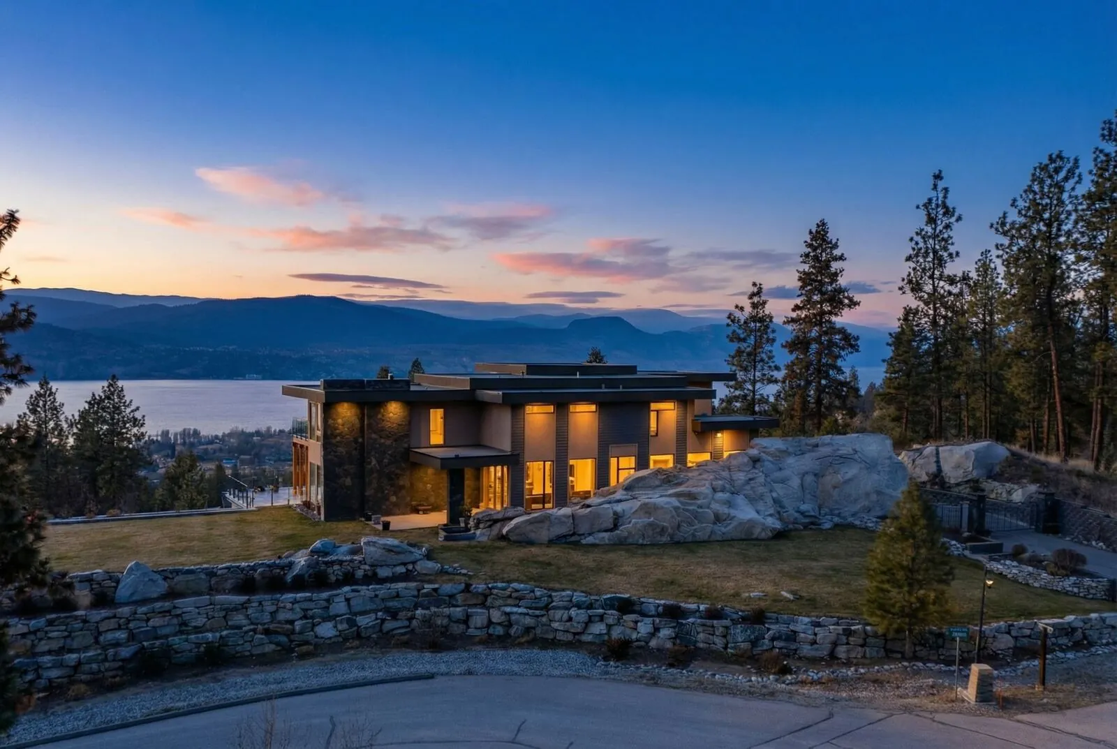 Modern hillside home glowing from within at twilight with a lake and mountains behind it