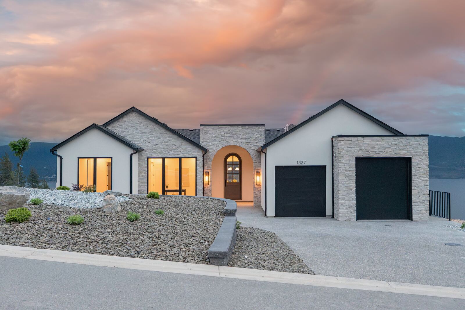 Stone and stucco bungalow with an arched front door and double garage glowing at sunset, lake in the distance