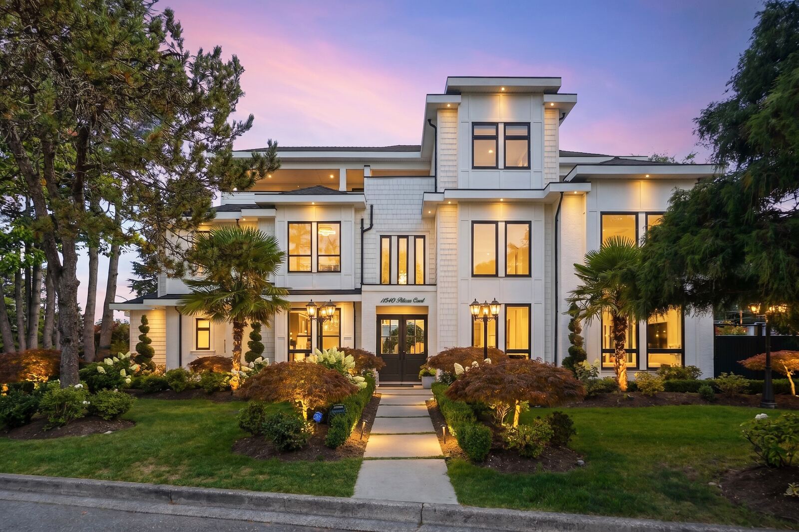 White two-storey home at dusk with lit windows, landscaped garden path and a pink and purple sky